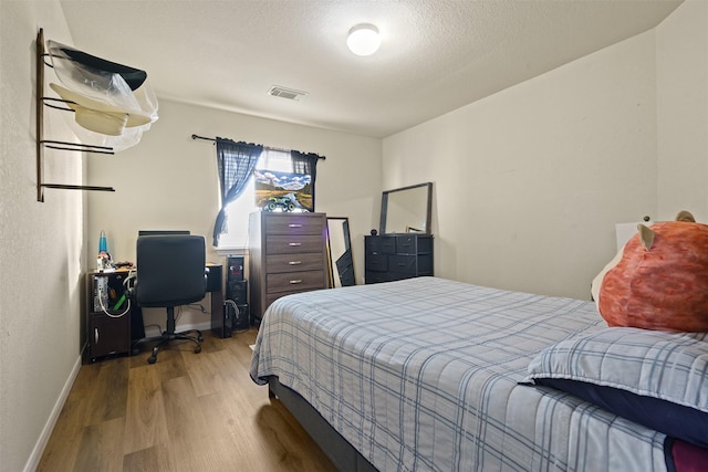 bedroom with baseboards, wood finished floors, and visible vents