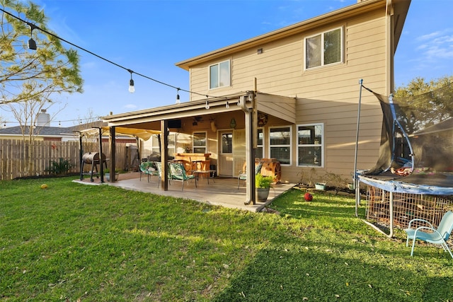 back of house with a lawn, a patio, a fenced backyard, and a trampoline