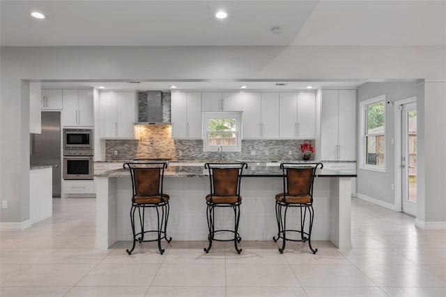 kitchen featuring backsplash, stainless steel appliances, baseboards, and wall chimney exhaust hood