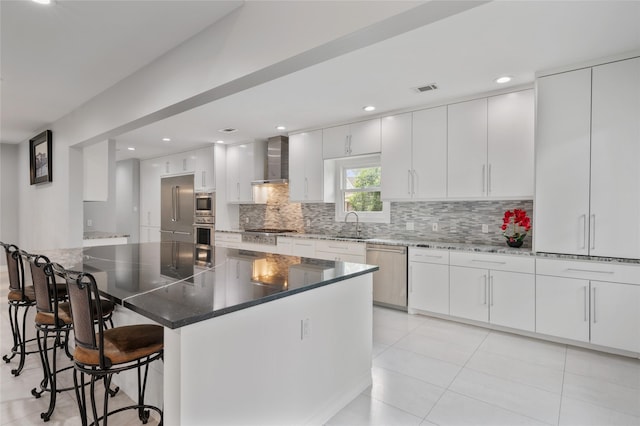 kitchen featuring wall chimney range hood, appliances with stainless steel finishes, a sink, a kitchen bar, and backsplash