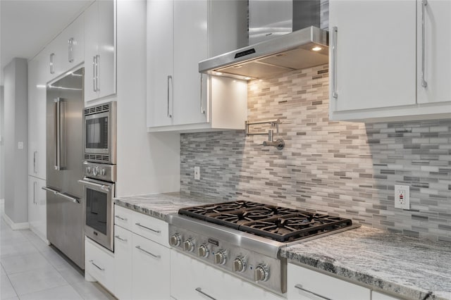 kitchen featuring light stone counters, white cabinets, stainless steel appliances, and wall chimney exhaust hood