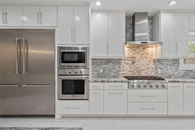 kitchen featuring wall chimney range hood, built in appliances, light tile patterned floors, and light stone countertops