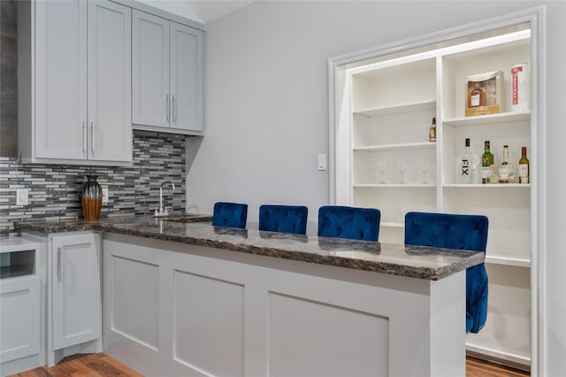 kitchen featuring backsplash, open shelves, a sink, dark stone countertops, and light wood-style flooring