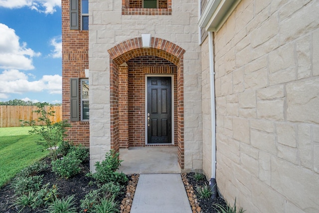 doorway to property with brick siding, fence, and stone siding