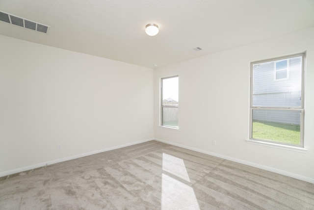 empty room with baseboards, visible vents, and light carpet