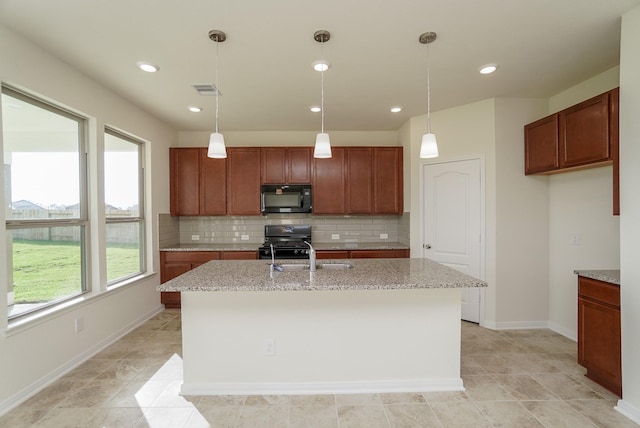 kitchen with a kitchen island with sink, light stone counters, black appliances, and tasteful backsplash