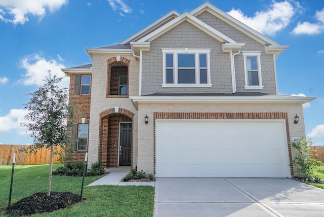 view of front of house featuring a front lawn, fence, stone siding, an attached garage, and driveway