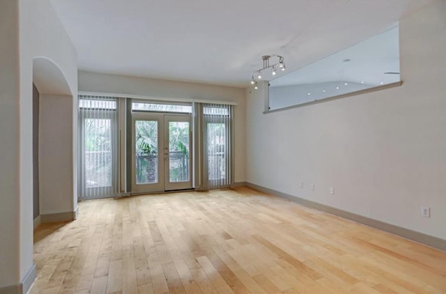 unfurnished room featuring arched walkways, baseboards, and wood finished floors