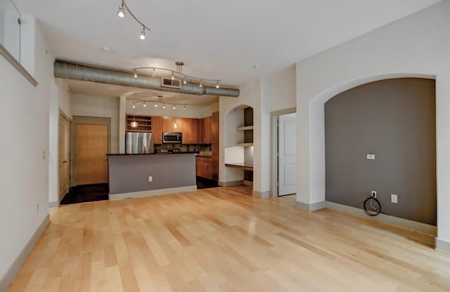 unfurnished living room with visible vents, track lighting, baseboards, arched walkways, and light wood finished floors