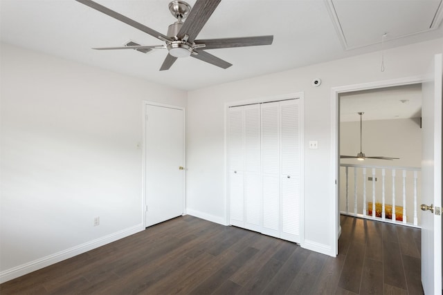 unfurnished bedroom featuring dark wood-type flooring, attic access, baseboards, and a closet