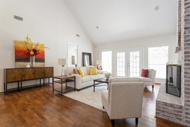 living area featuring high vaulted ceiling, a brick fireplace, wood finished floors, and visible vents