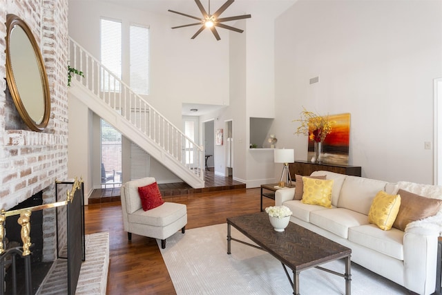 living area featuring a fireplace, a ceiling fan, wood finished floors, a towering ceiling, and stairway
