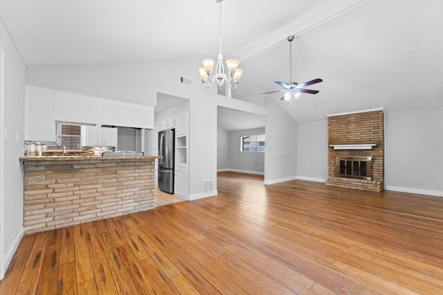unfurnished living room with visible vents, a fireplace, baseboards, light wood finished floors, and ceiling fan with notable chandelier