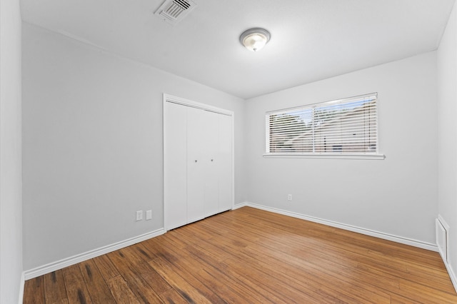 unfurnished bedroom featuring visible vents, baseboards, wood finished floors, and a closet