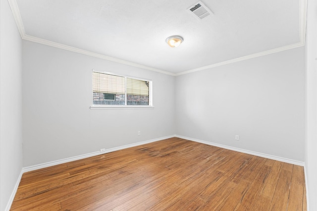empty room with crown molding, baseboards, wood finished floors, and visible vents