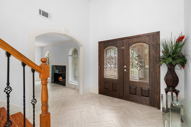 foyer with a lit fireplace, visible vents, arched walkways, baseboards, and a high ceiling