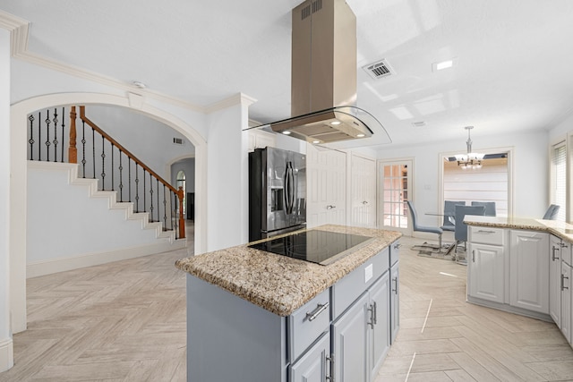 kitchen with island exhaust hood, visible vents, black electric stovetop, a notable chandelier, and stainless steel fridge