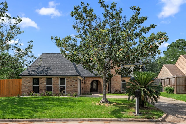 english style home featuring fence, a front yard, roof with shingles, and brick siding