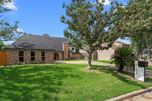 view of front of house featuring fence, a shingled roof, brick siding, and a front yard