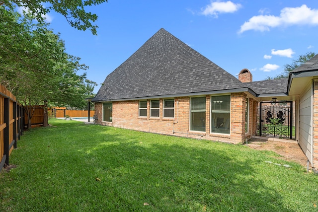 rear view of house with a yard, brick siding, a fenced backyard, and roof with shingles