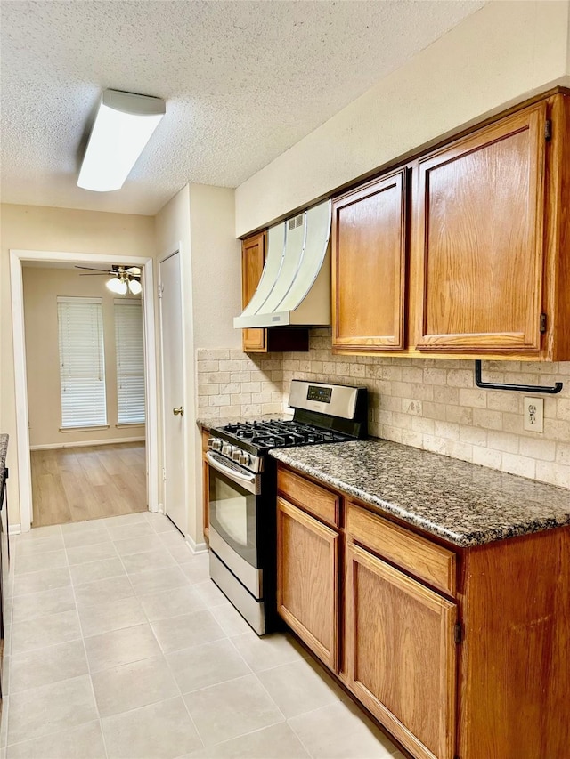 3022 Sam Houston Dr, Sugar Land, TX 77479 - kitchen with stainless steel gas range oven, custom range hood, backsplash, brown cabinets, and a textured ceiling
