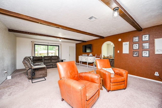 living room with a textured ceiling, light colored carpet, visible vents, arched walkways, and beam ceiling