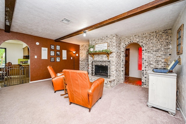 carpeted living area with a fireplace, beamed ceiling, a textured ceiling, and visible vents