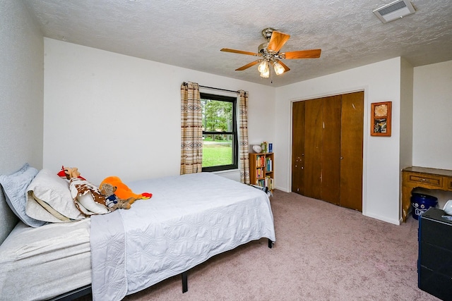 carpeted bedroom featuring a textured ceiling, ceiling fan, visible vents, and baseboards