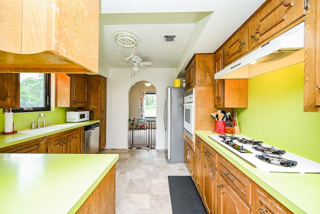 kitchen with ceiling fan, arched walkways, under cabinet range hood, a sink, and appliances with stainless steel finishes