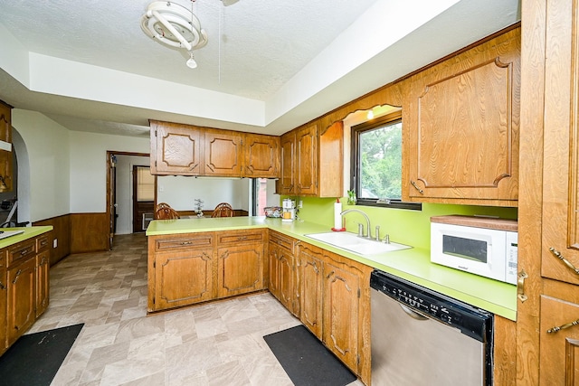 kitchen featuring brown cabinetry, dishwasher, a sink, light countertops, and white microwave