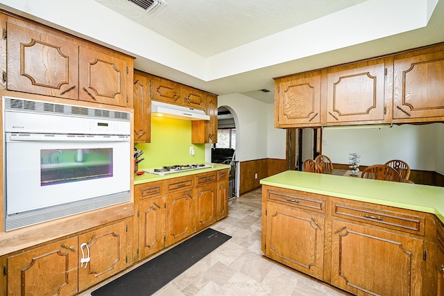 kitchen with visible vents, white appliances, under cabinet range hood, brown cabinets, and arched walkways