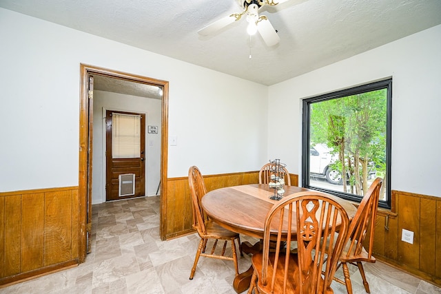 dining area with a wainscoted wall, a ceiling fan, wood walls, and a textured ceiling