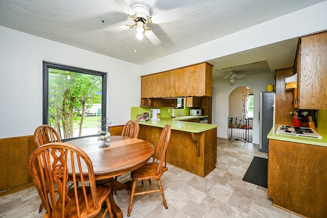 dining room featuring a healthy amount of sunlight, arched walkways, ceiling fan, and stone finish flooring