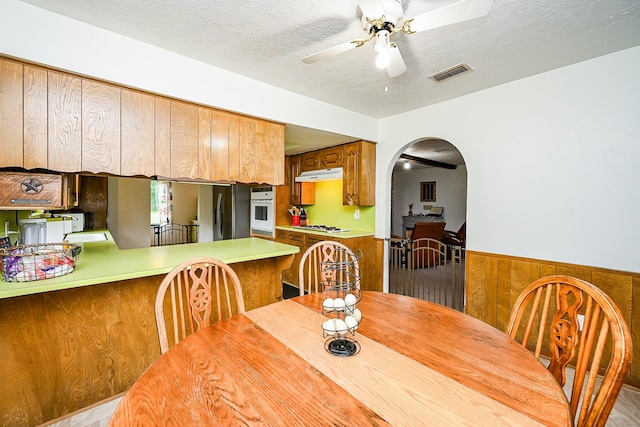 dining area featuring visible vents, wood walls, ceiling fan, a wainscoted wall, and arched walkways