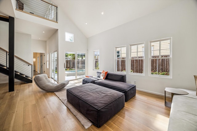 living area featuring stairs, high vaulted ceiling, baseboards, and light wood-style flooring