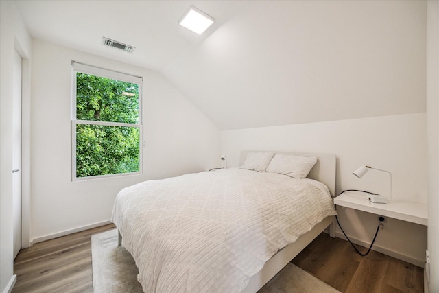 bedroom featuring baseboards, visible vents, wood finished floors, and vaulted ceiling