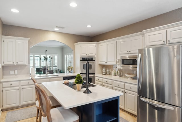 kitchen featuring appliances with stainless steel finishes, arched walkways, decorative backsplash, a kitchen island, and visible vents