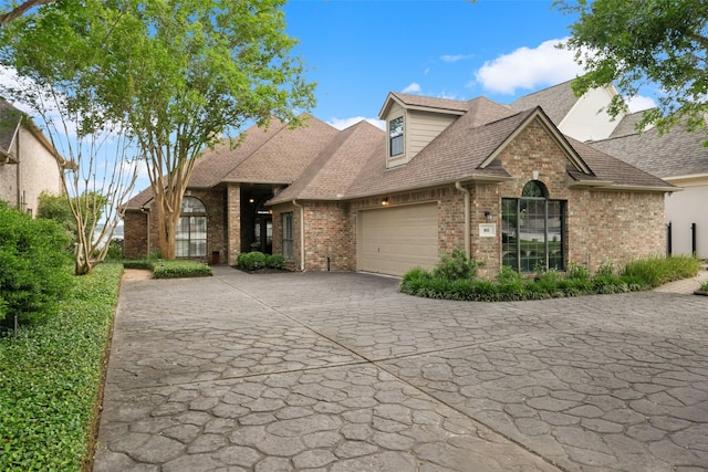 view of front of house with a garage, driveway, roof with shingles, and brick siding
