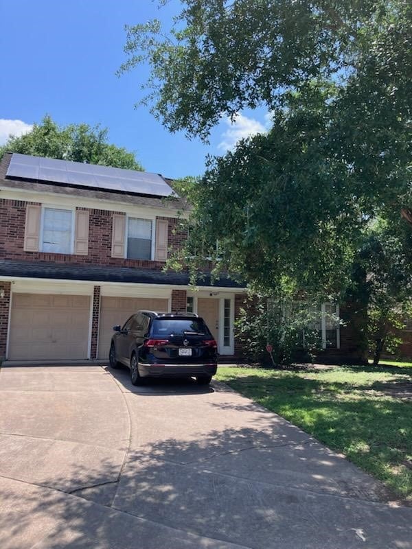 view of front facade featuring a garage, brick siding, driveway, and solar panels
