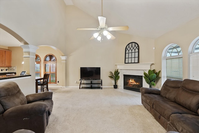 living area with ceiling fan, light carpet, arched walkways, decorative columns, and a fireplace with flush hearth