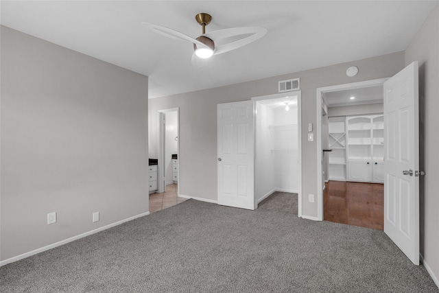 unfurnished bedroom with carpet floors, visible vents, baseboards, a walk in closet, and ceiling fan