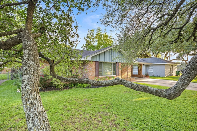 ranch-style house featuring roof with shingles, board and batten siding, a front lawn, and brick siding