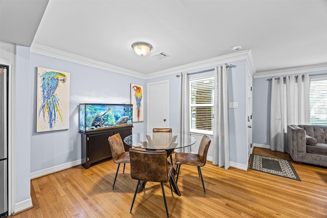 dining area featuring visible vents, baseboards, crown molding, and light wood-type flooring
