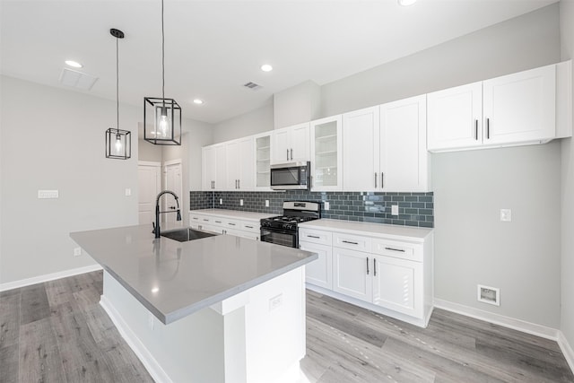 kitchen featuring a sink, visible vents, stainless steel microwave, gas range oven, and a center island with sink