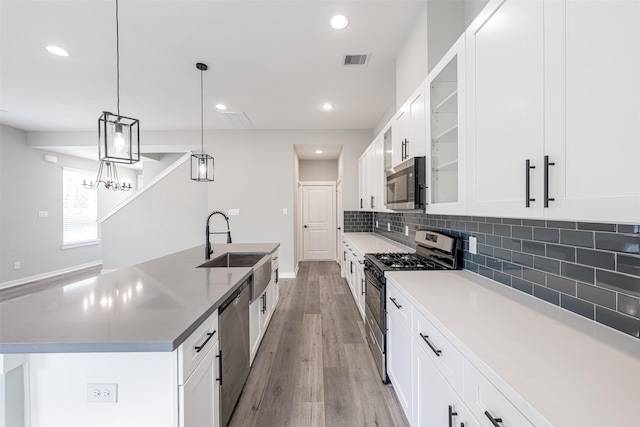 kitchen with visible vents, a center island with sink, a sink, appliances with stainless steel finishes, and backsplash