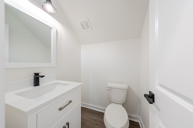 half bathroom with visible vents, vanity, lofted ceiling, wood finished floors, and toilet
