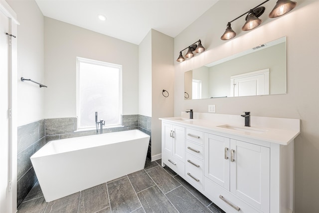 bathroom featuring double vanity, visible vents, a freestanding tub, tile walls, and a sink