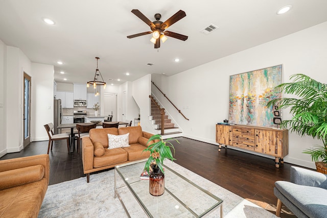 living area featuring light wood-style floors, baseboards, ceiling fan, and stairs