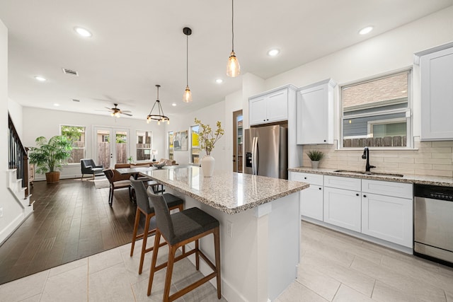 kitchen featuring appliances with stainless steel finishes, light stone counters, a sink, a center island, and open floor plan