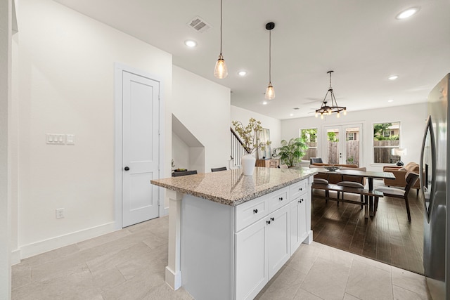 kitchen with decorative light fixtures, visible vents, light stone countertops, freestanding refrigerator, and white cabinetry